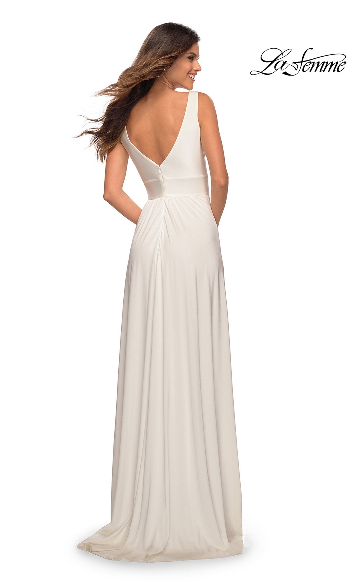 A woman in the La Femme Deep V-Neck Long A-Line Prom Dress 28547 stands facing away, showcasing its sleeveless, floor-length white design with a V-back, elegant A-line silhouette, and subtle waist pleating.
